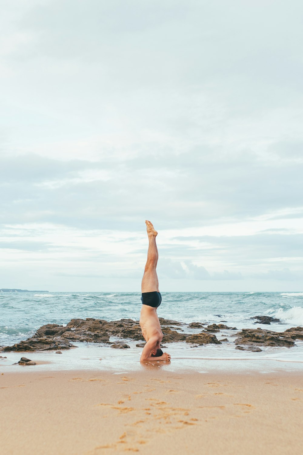 man in black shorts lying on brown rock near sea during daytime