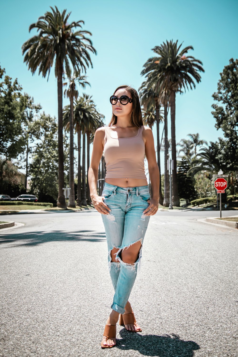 woman in white tank top and blue denim shorts standing on road during daytime
