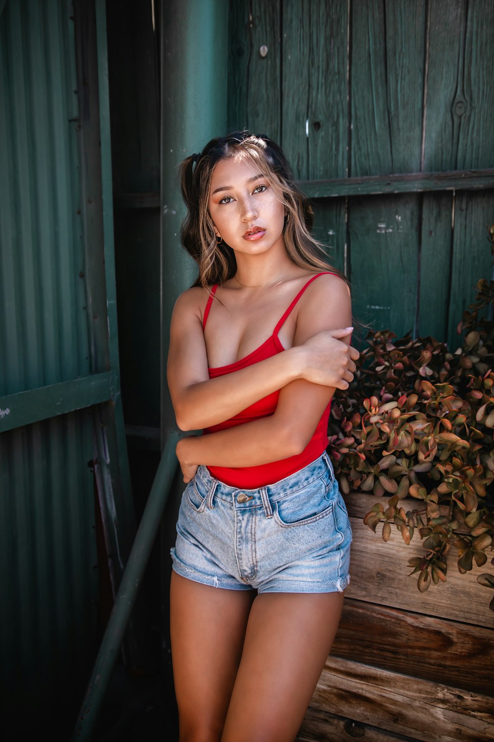 woman in red tank top and blue denim shorts standing near green wooden wall