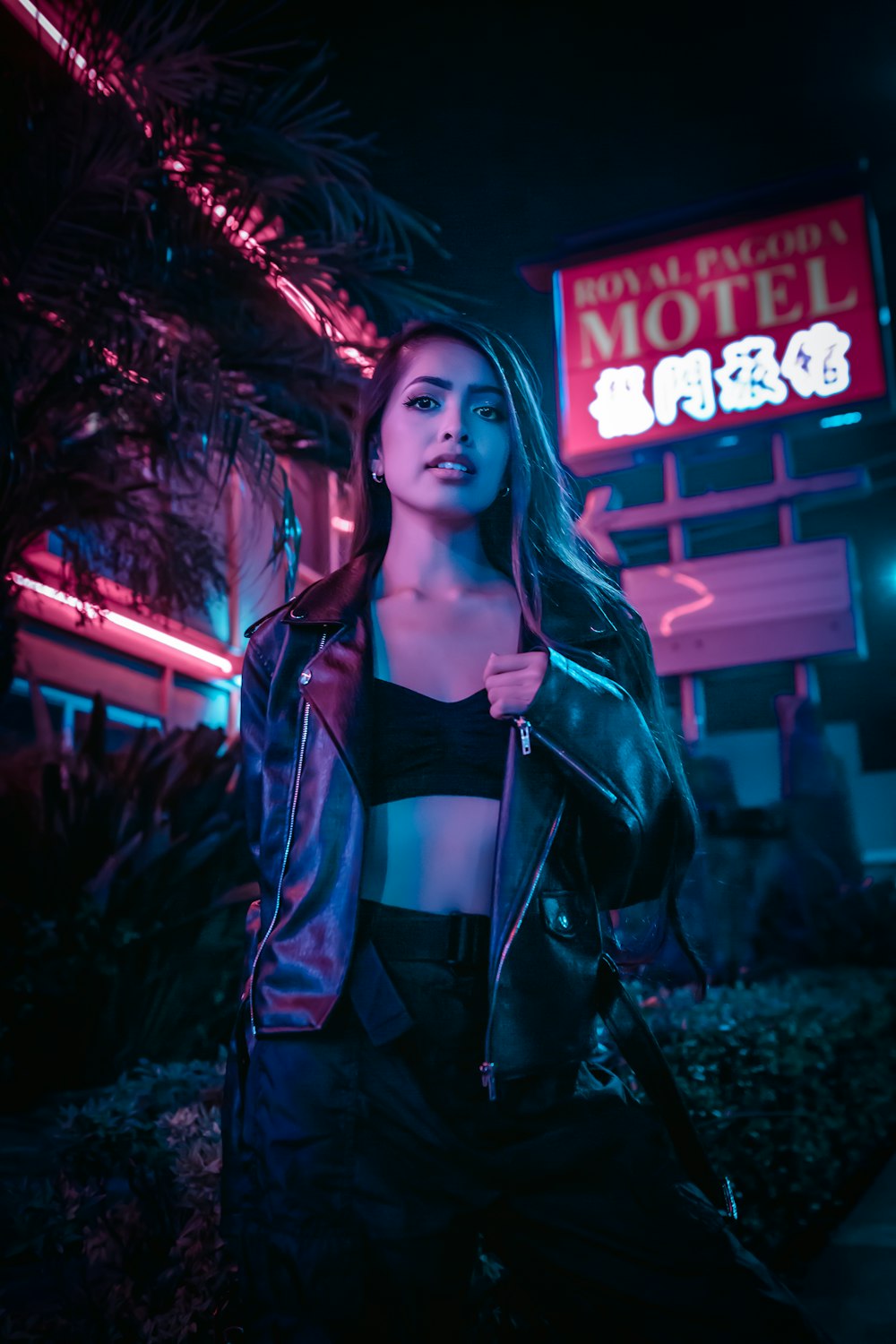 woman in black leather jacket standing near red and white neon signage during nighttime