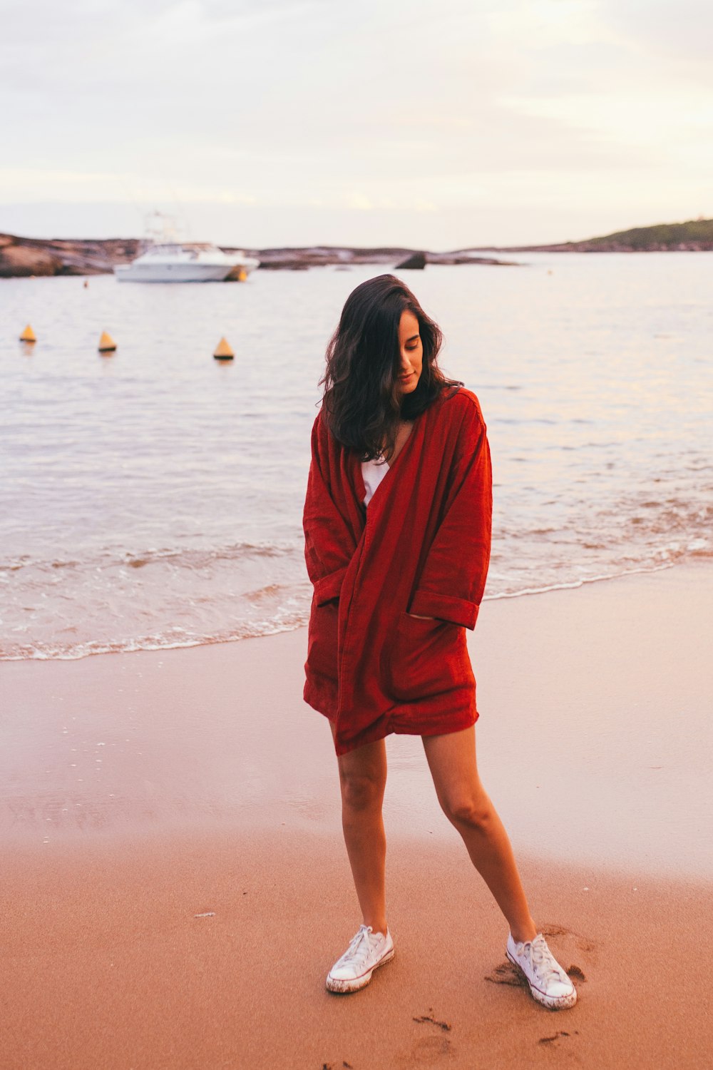 昼間のビーチに立つ赤い長袖の女性