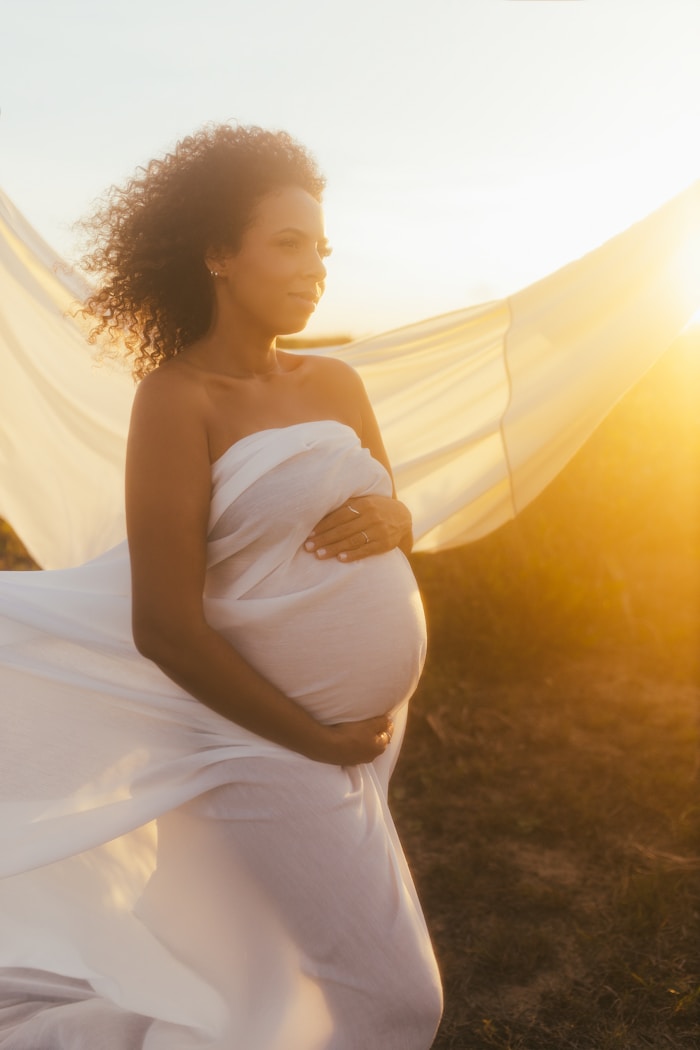 Black pregnant woman standing outdoors in white