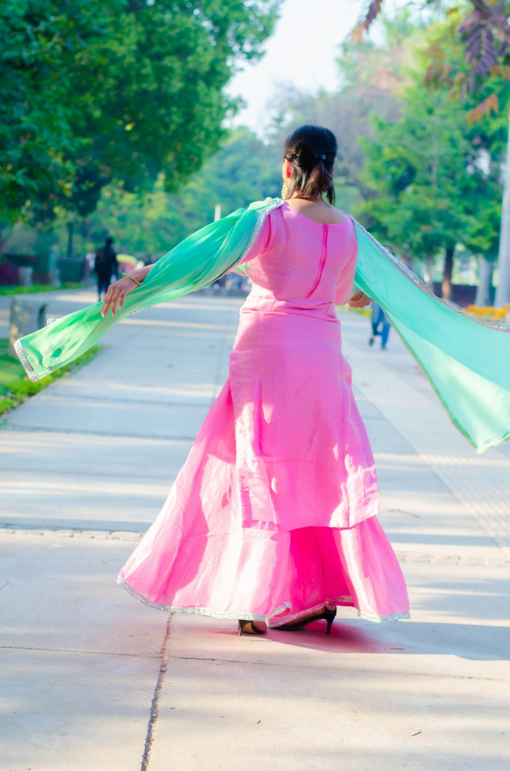 woman in pink dress holding green and blue scarf walking on street during daytime