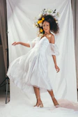Editorial-style shot of a model draped in a flowing white dress against a dark beige textured wall.