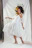 Elegant model showcasing a flowing cream dress with subtle gold jewelry in a softly lit studio.