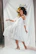 Elegant model showcasing a flowing cream dress with subtle gold jewelry in a softly lit studio.