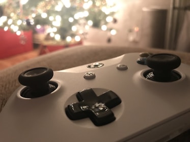 A close-up of a gaming controller with an illuminated background featuring soft, out-of-focus lights, likely from a decorated tree or holiday setup.