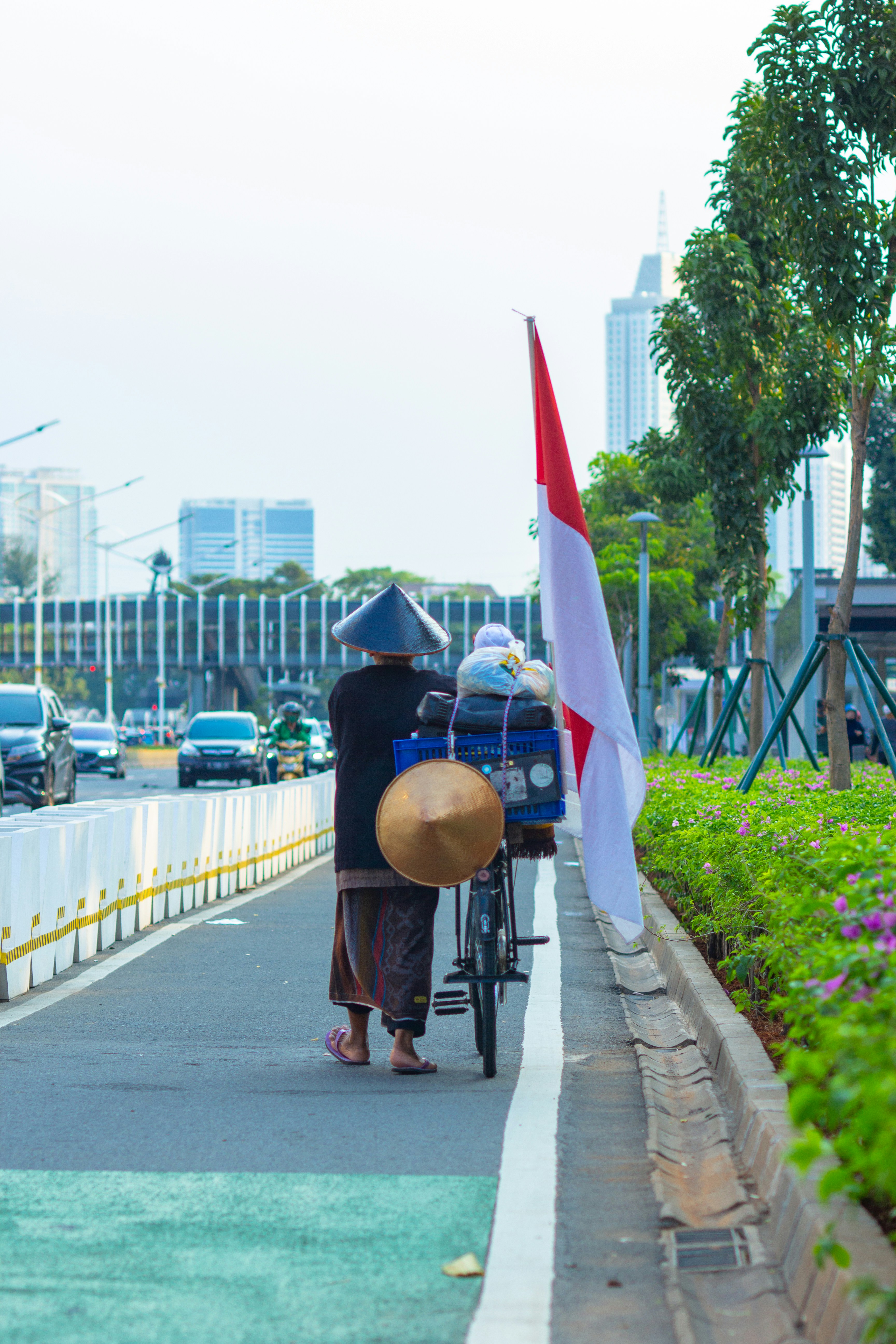 Pria bertopi coklat dan jaket hitam berjalan di trotoar dengan bendera di samping selama