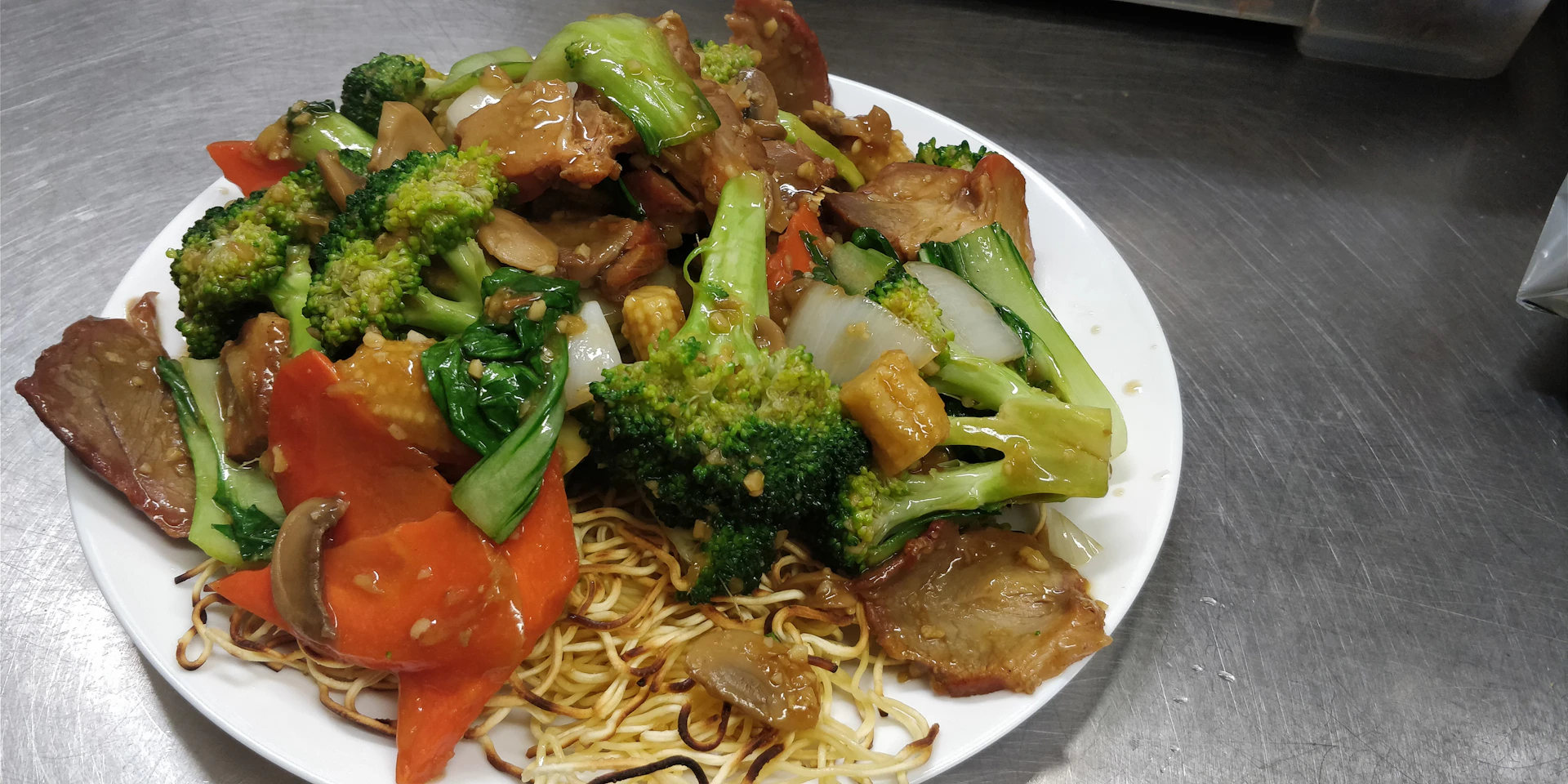 A vibrant close-up of sizzling Asian fusion stir-fry with colorful vegetables and tender meat glazed in a glossy sauce.