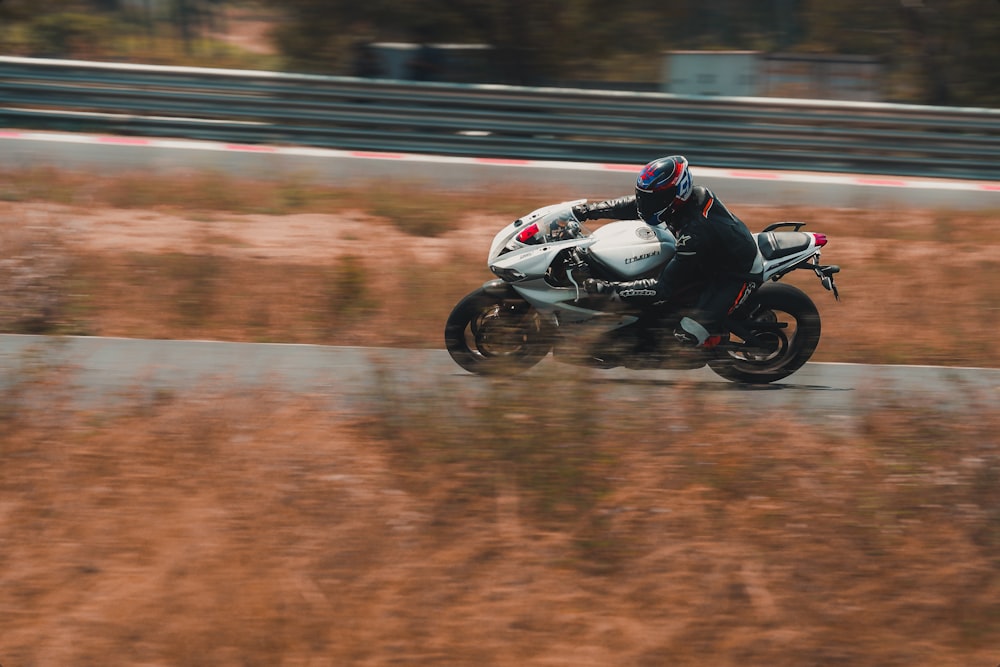 man riding white and black sports bike on track field during daytime