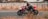 A motorcyclist wearing a black helmet and gear rides a red and white sports motorcycle at high speed on a racetrack. The background is slightly blurred, indicating fast motion, and dry grass is visible in the foreground.