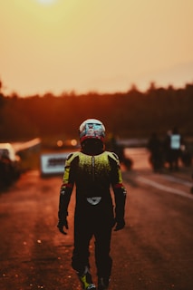 A rider wearing a custom leather racing suit, standing beside a classic motorcycle at sunset.