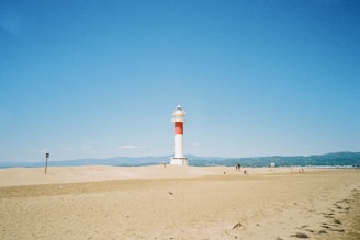 white and red lighthouse on brown sand under blue sky during daytime