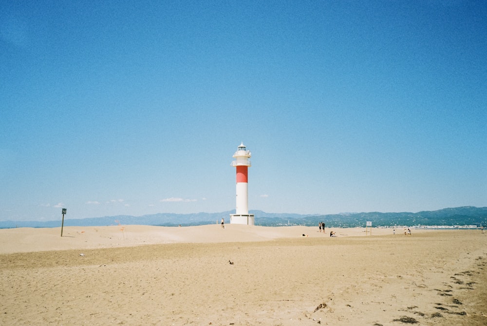 white and red lighthouse on brown sand under blue sky during daytime