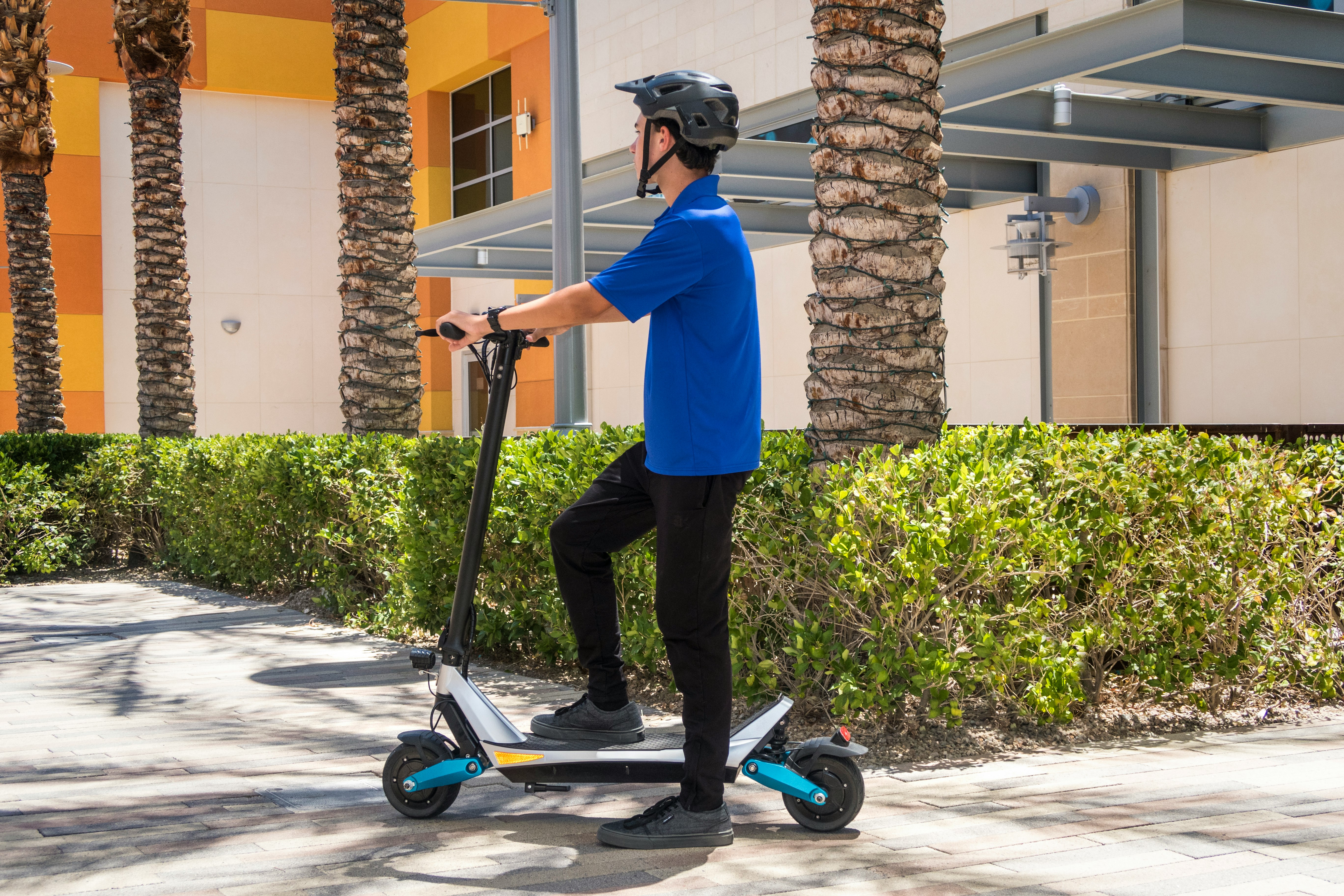 man in blue dress shirt and black pants riding blue and black kick scooter during daytime