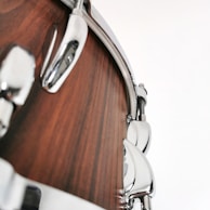 Close-up view of a drum with a polished wooden finish and shiny metallic hardware, including lugs and tension rods.