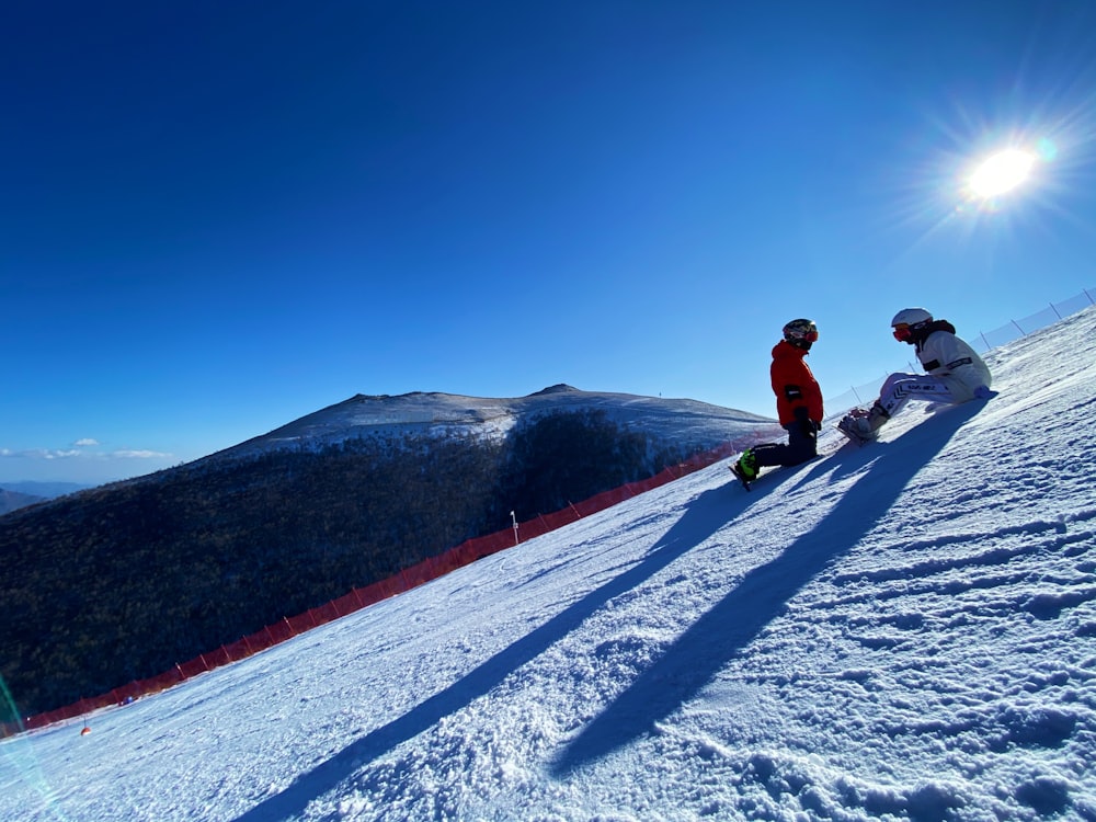 2 men in red jacket and black pants riding ski blades on snow covered mountain during