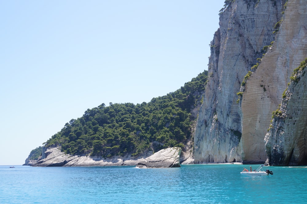 people riding boat on sea near gray rock formation during daytime