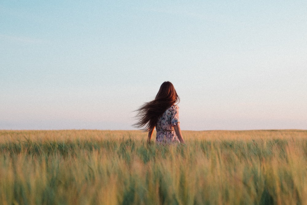 woman in brown and white floral dress standing on green grass field during daytime