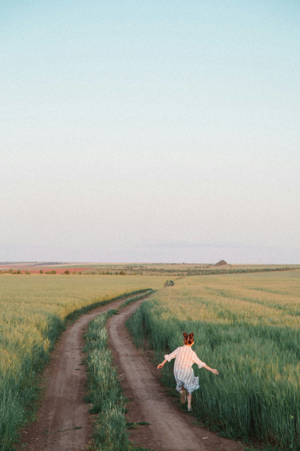 하얀 드레스 셔츠를 입은 남자가 낮에 푸른 잔디밭 사이의 갈색 흙길을 걷고 있다