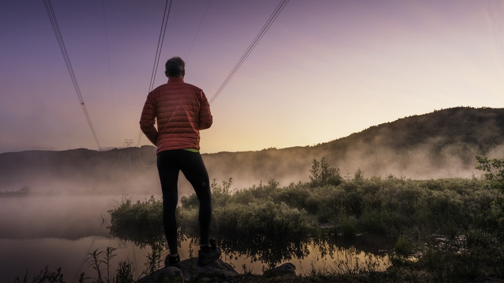 man in red shirt and black pants standing on rock during daytime