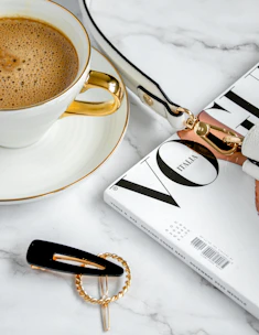 A compact beige crossbody bag placed on a marble countertop with a cup of coffee beside it.