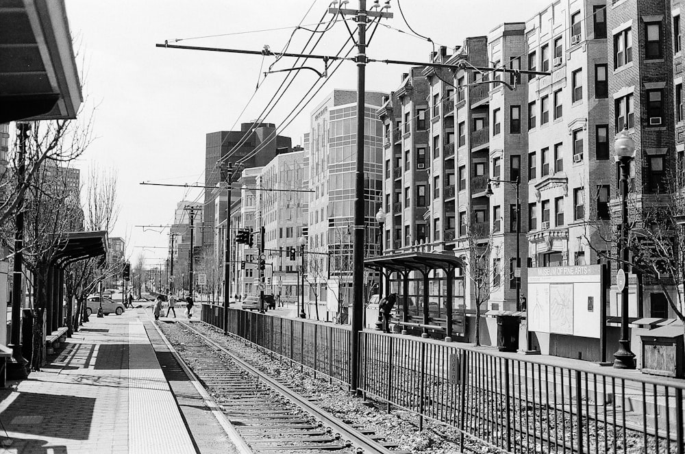 grayscale photo of train rail near buildings