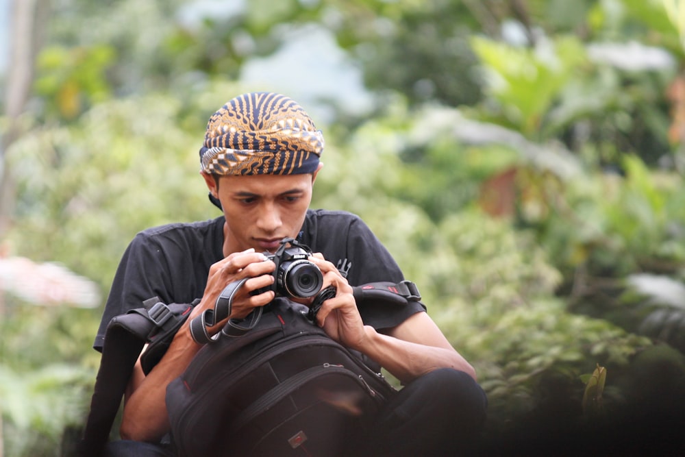 Hombre con camisa negra y gorra de punto marrón sosteniendo una cámara DSLR negra