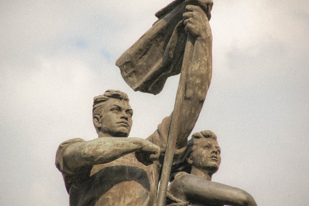 grayscale photo of man holding stick statue