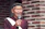 An elderly man speaking thoughtfully into a microphone, surrounded by family photos.