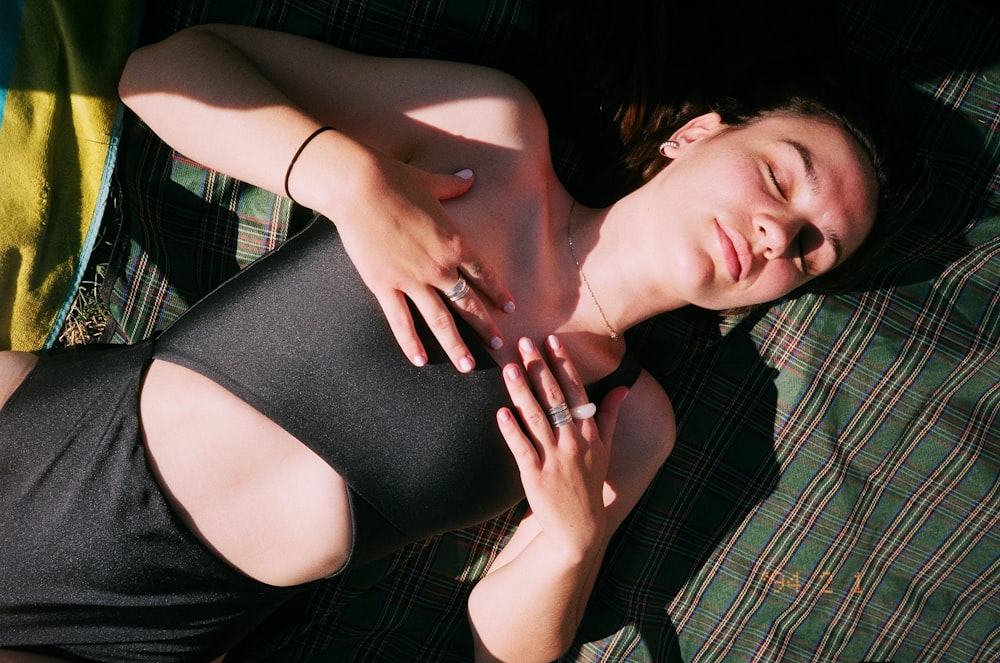 woman in black tank top lying on green and black plaid textile