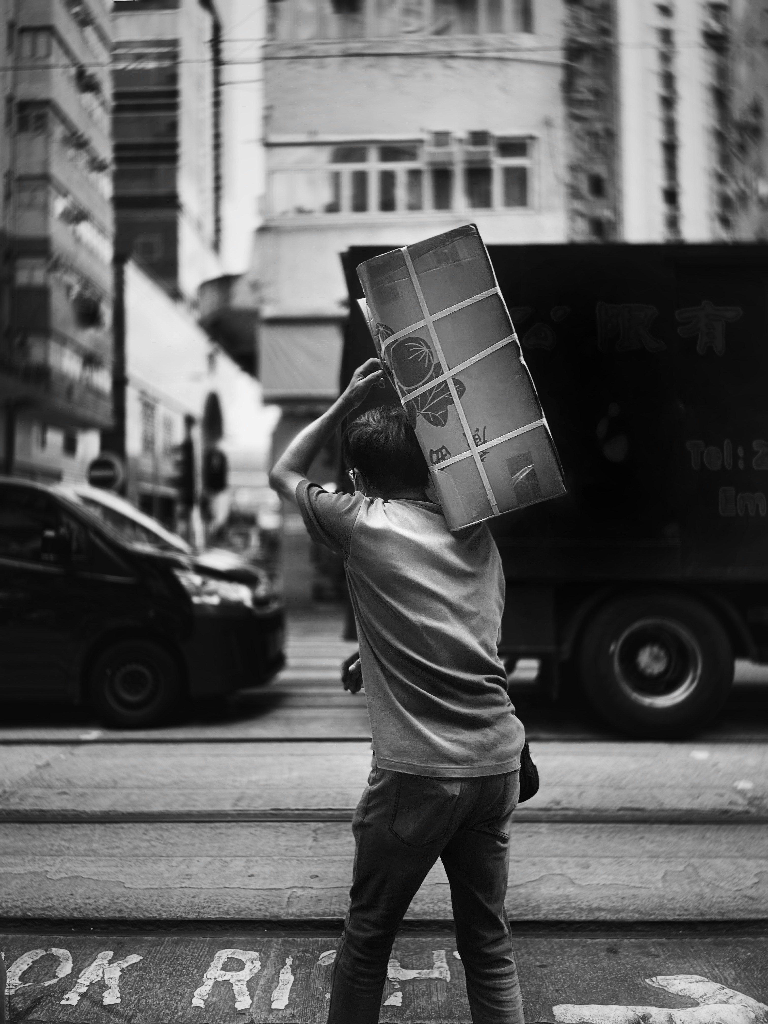 man in t-shirt and pants carrying box in grayscale photography