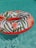 A colorful inflatable ring with a floral pattern floats on the clear blue water of a pool. The ring is decorated with orange and pink flowers and green leaves, creating a vibrant contrast against the water.