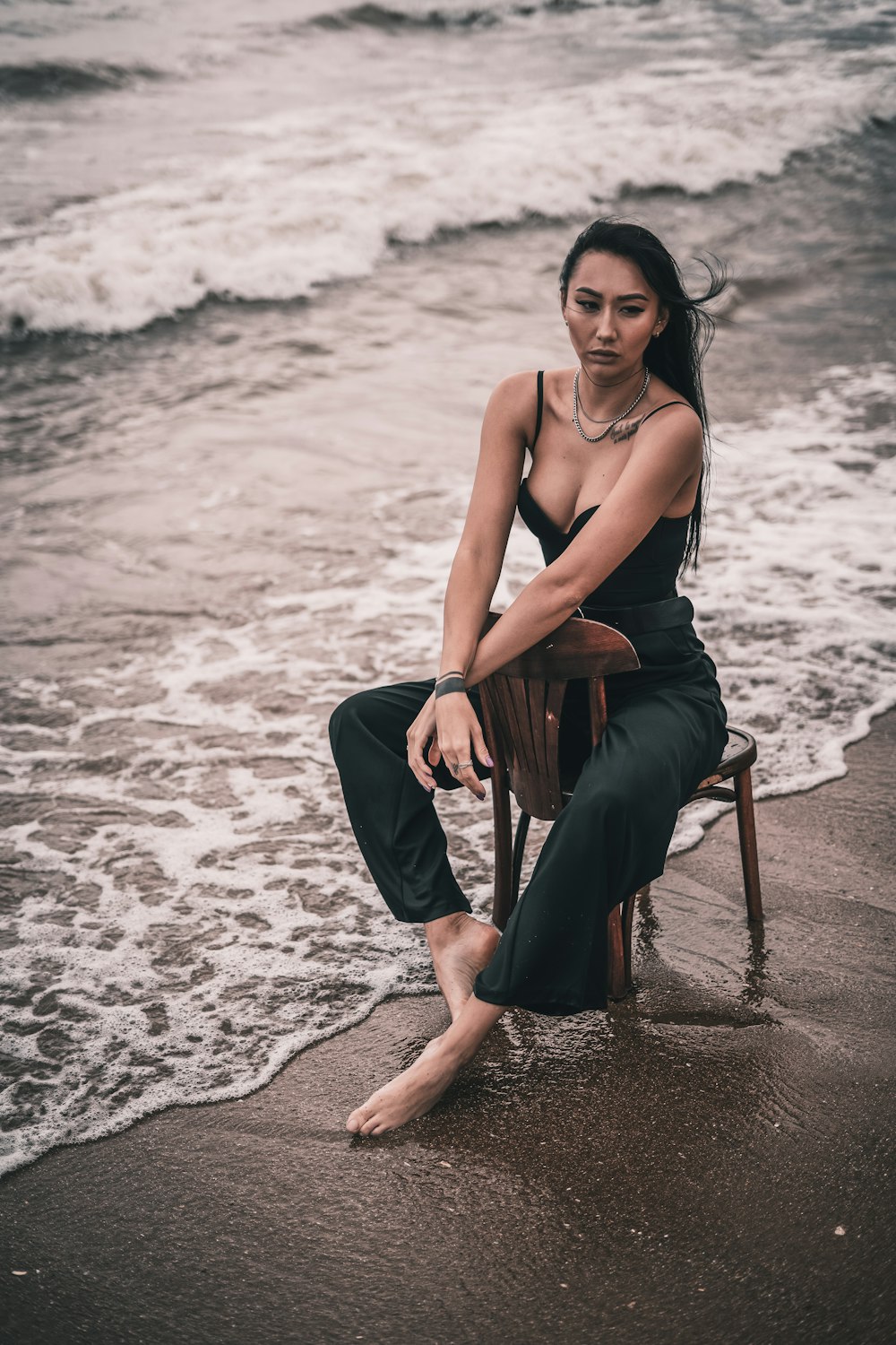 woman in black tank top sitting on brown wooden seat on beach during daytime