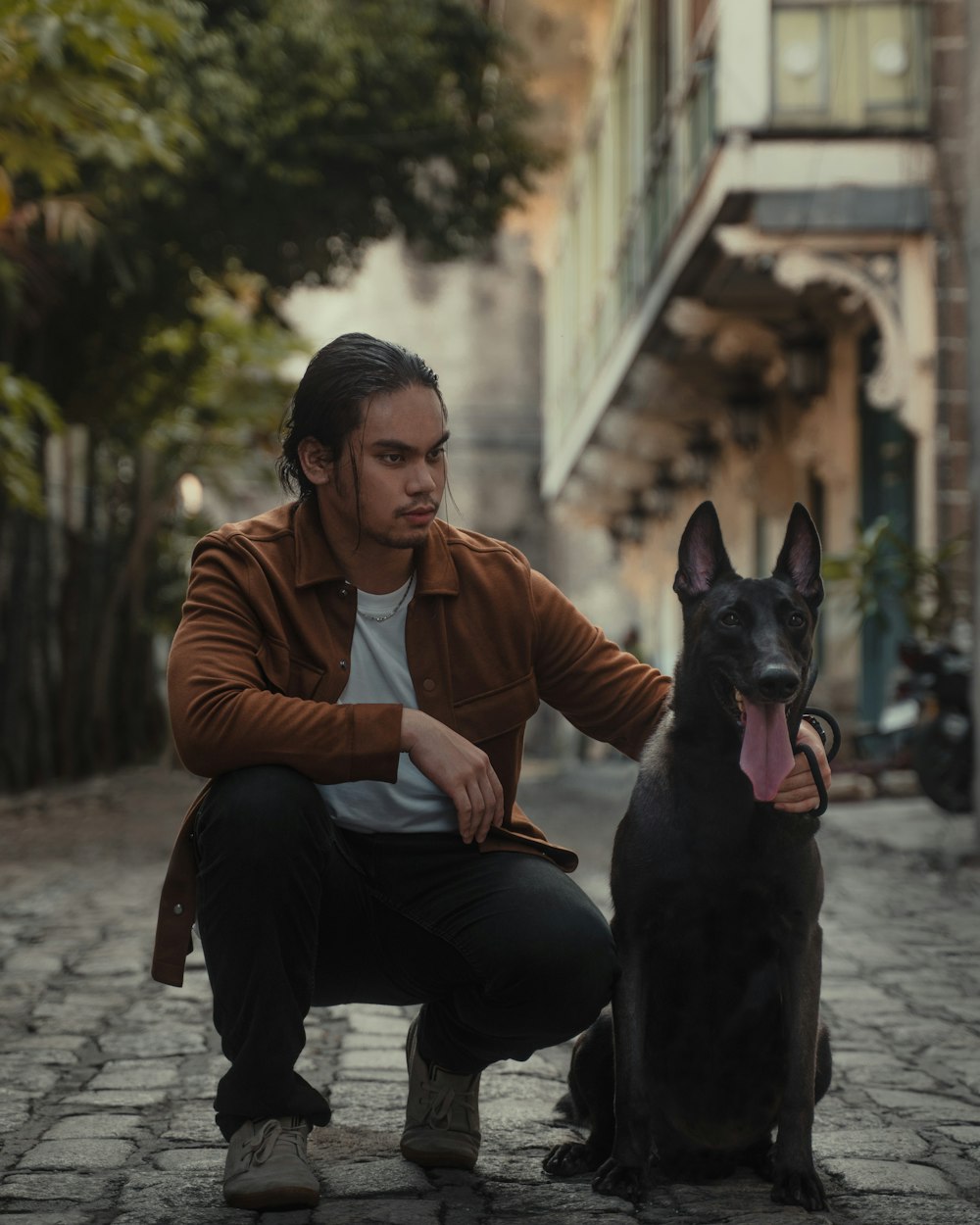 man in brown polo shirt and black pants sitting beside black short coated dog