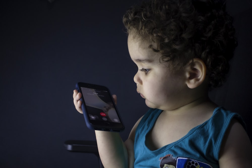 boy in blue tank top holding black smartphone