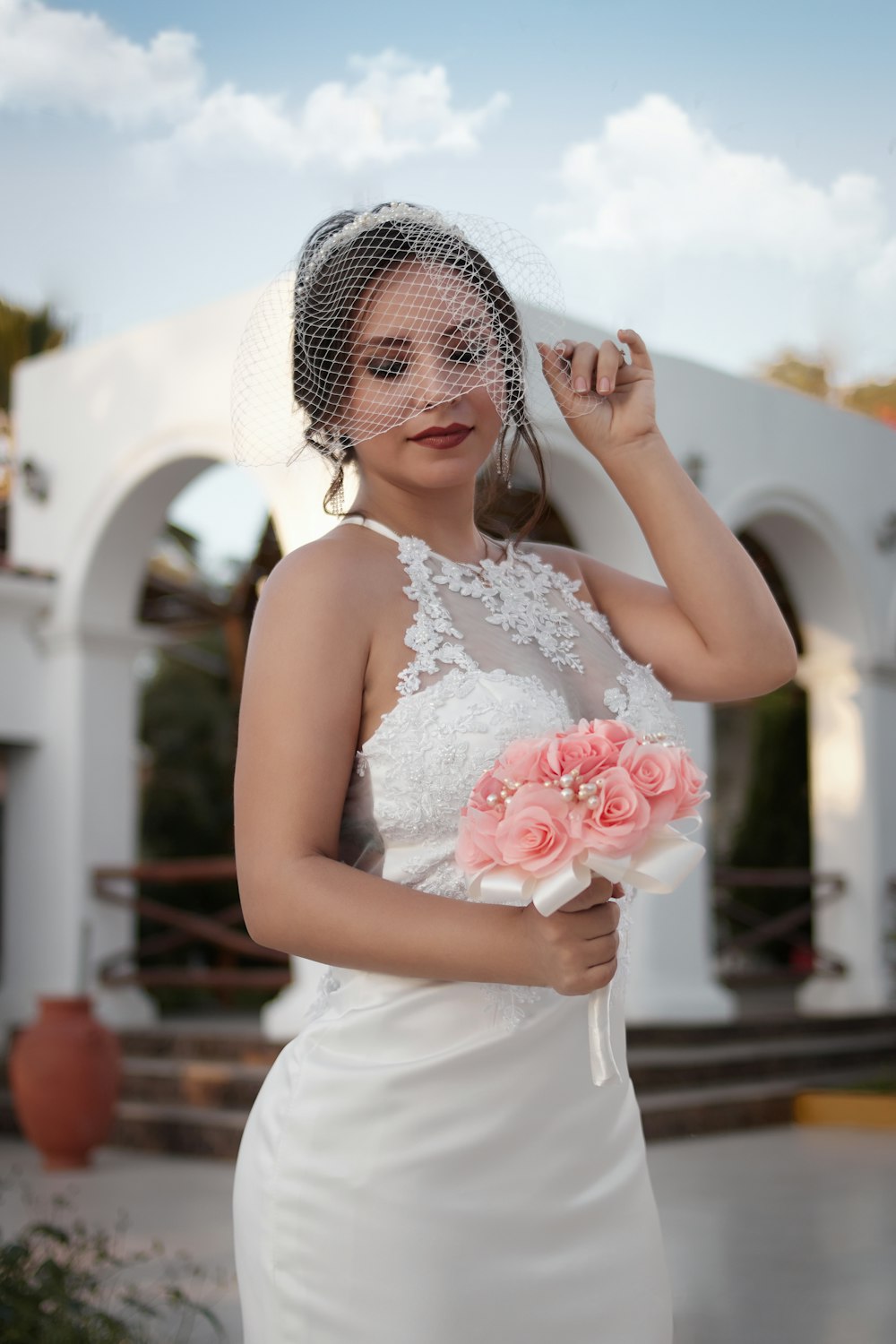 Mujer en vestido blanco sin mangas sosteniendo ramo de rosas rojas