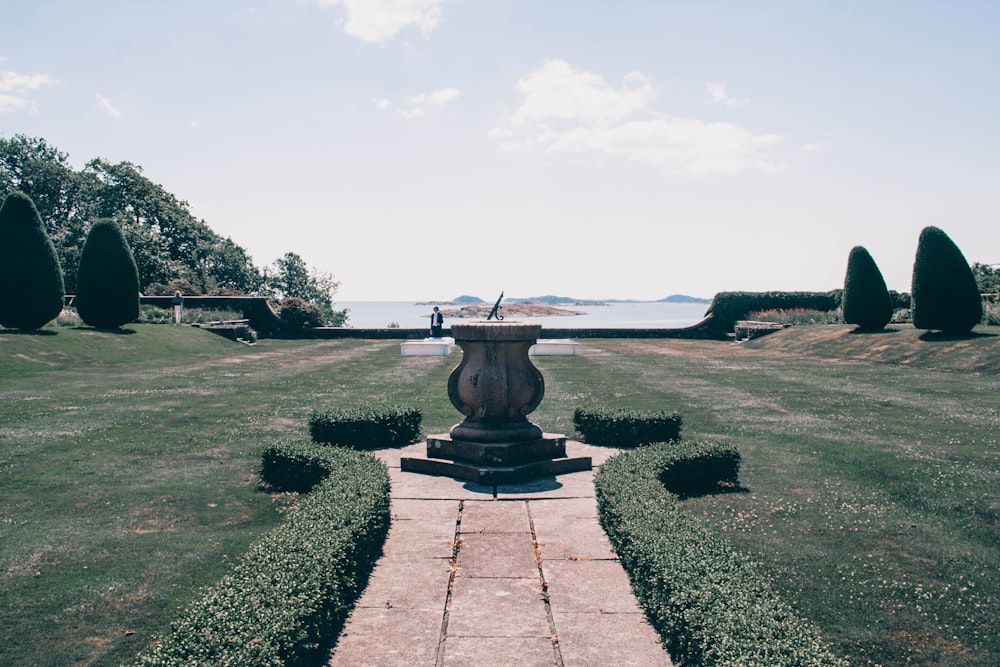 gray concrete round outdoor fountain surrounded by green grass field under white sky during daytime