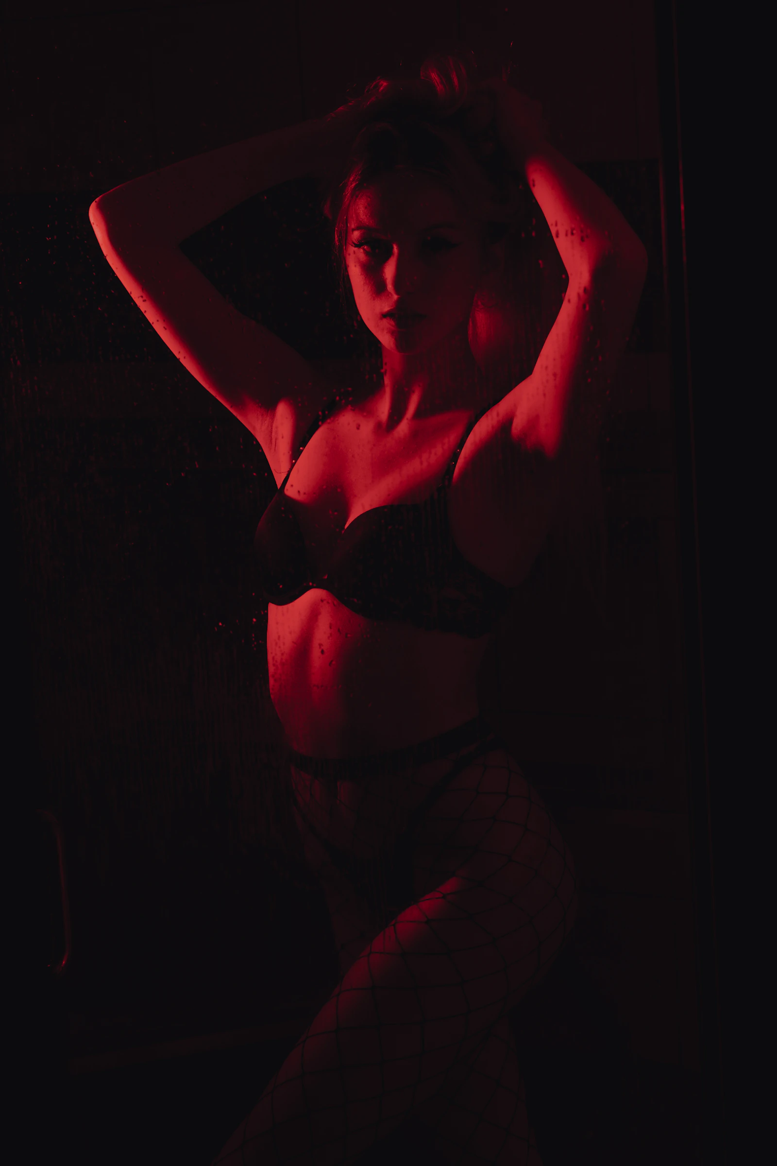 Low-key boudoir portrait of a woman in lingerie against deep shadow, lit by a single warm source.