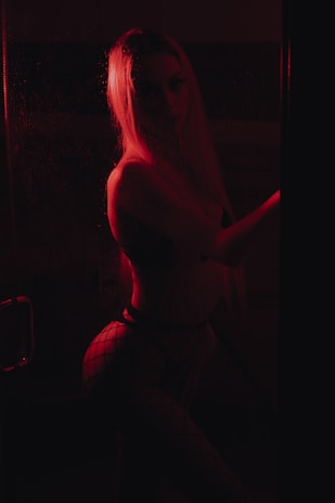 A close-up of a cam girl playfully teasing in ambient red lighting.