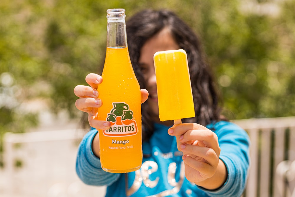 person holding clear glass bottle with orange juice