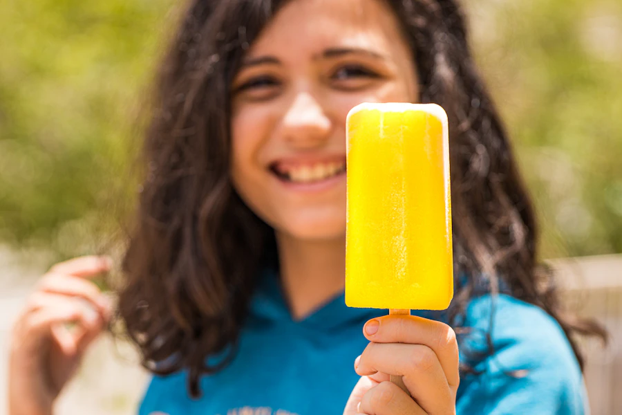 A smiling girl holding a mango ice stick