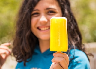 woman in blue shirt holding yellow ice pop