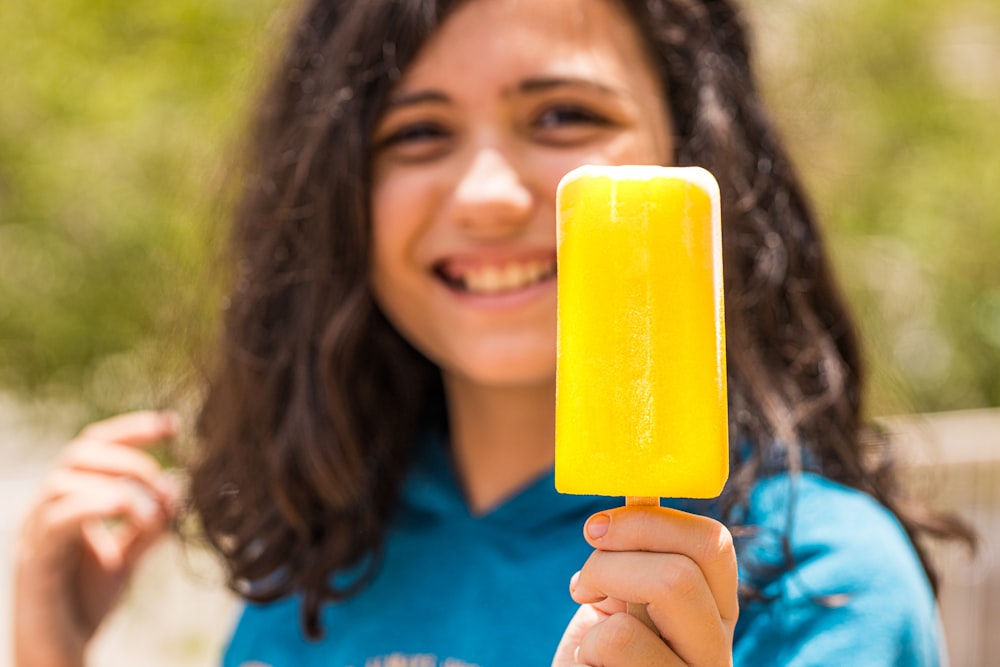woman in blue shirt holding yellow ice pop