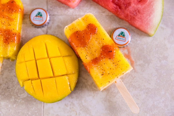 A vibrant close-up of a mango fruit popsicle melting slightly under the sun.