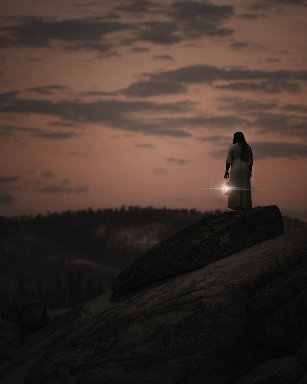 person in white hoodie sitting on gray rock during daytime