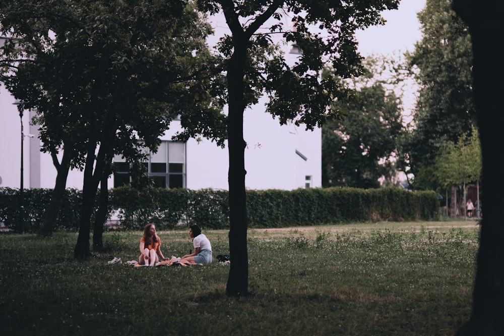 woman in white shirt sitting on green grass field near green tree during daytime