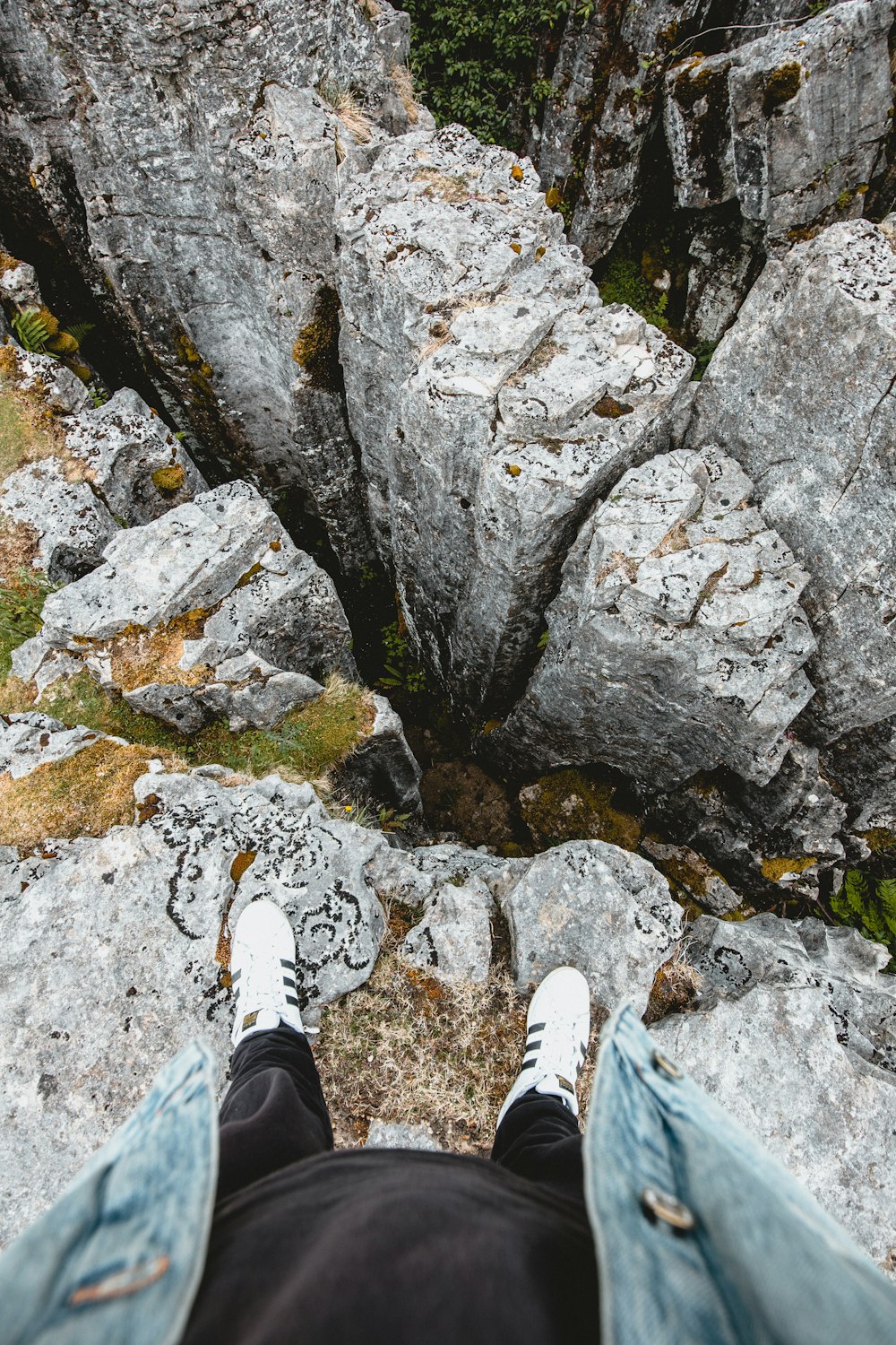 person in white sneakers standing on rocky hill