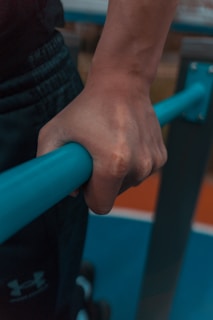 A close-up of a hand gripping a blue exercise bar, with a background of gym equipment.