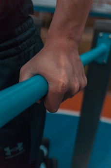 A close-up of a hand gripping a blue exercise bar, with a background of gym equipment.